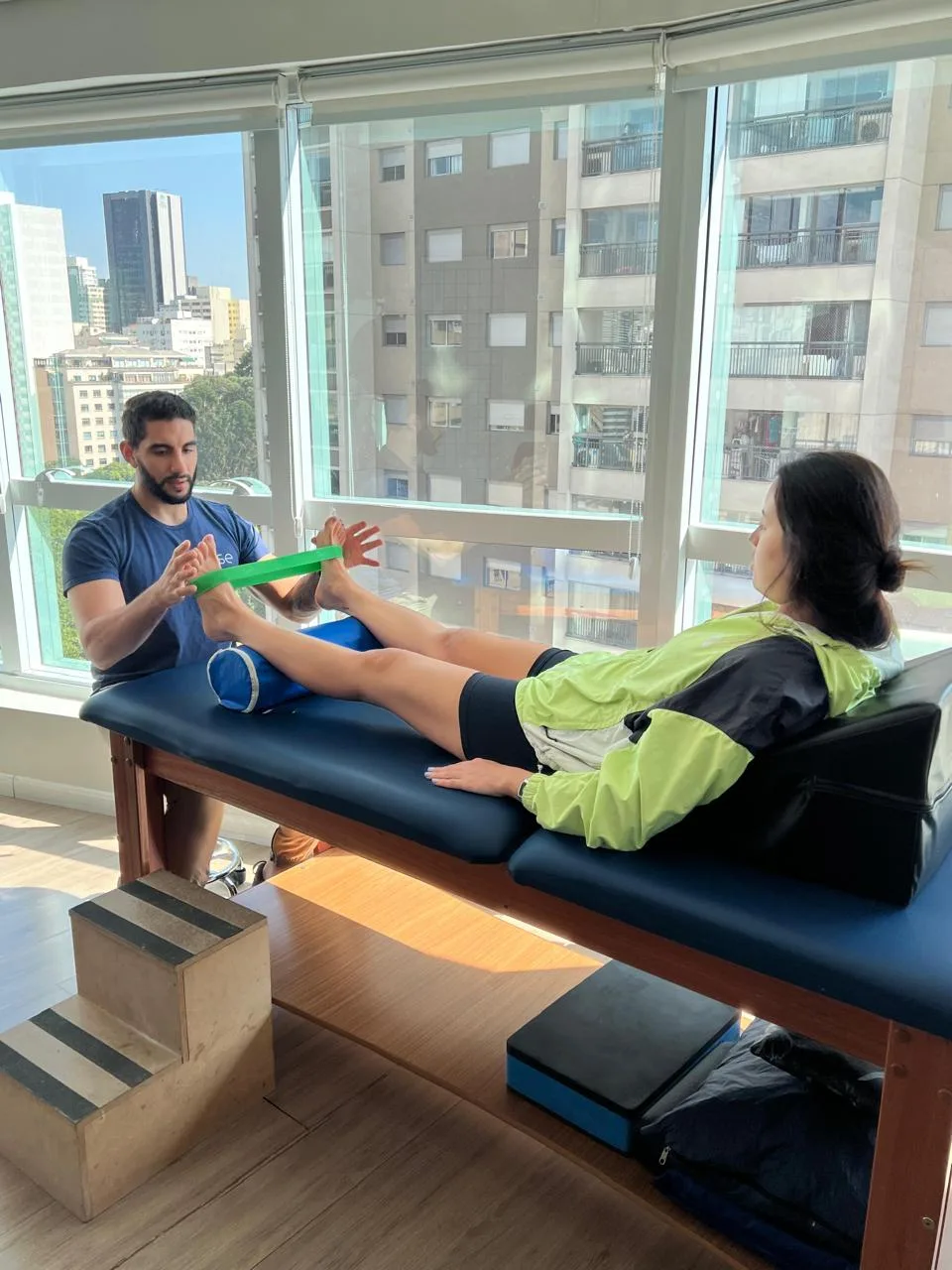 Fisioterapeuta conduzindo exercício de mobilidade de tornozelo com faixa elástica durante sessão na Boese
